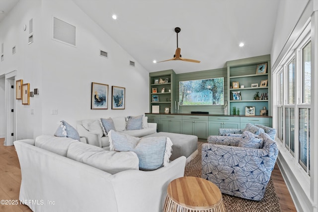 living room featuring ceiling fan, built in features, high vaulted ceiling, and light hardwood / wood-style flooring