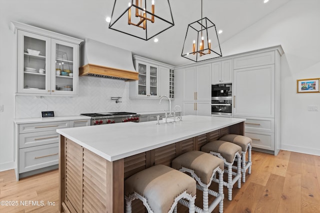 kitchen featuring a kitchen breakfast bar, backsplash, pendant lighting, a kitchen island with sink, and custom range hood