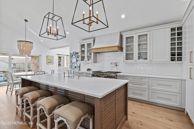 kitchen featuring a center island with sink, custom exhaust hood, a breakfast bar, and vaulted ceiling