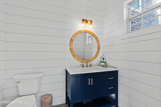 bathroom featuring vanity, toilet, and wooden walls