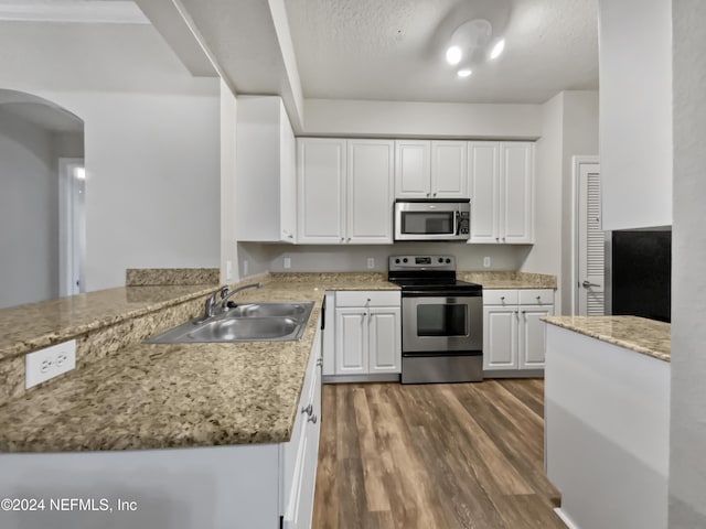 kitchen with sink, stainless steel appliances, light stone counters, kitchen peninsula, and white cabinets