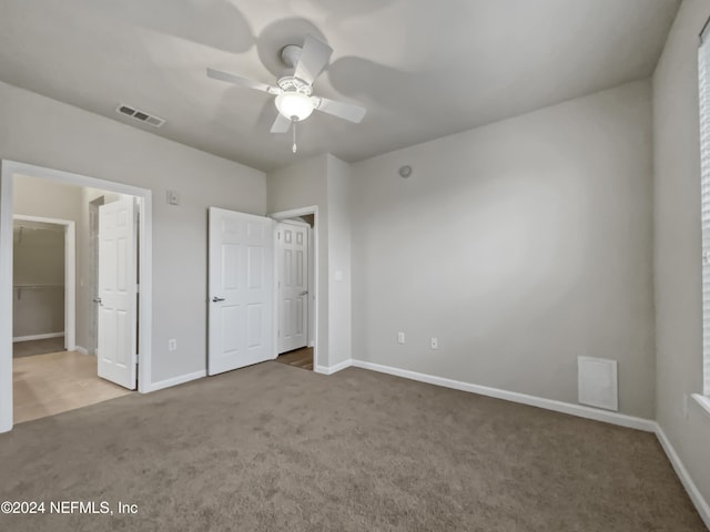 unfurnished bedroom with carpet flooring, ceiling fan, a walk in closet, and a closet