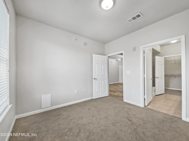 unfurnished bedroom featuring a spacious closet, a closet, and light carpet