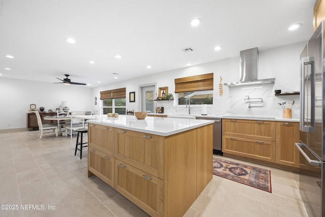 kitchen featuring appliances with stainless steel finishes, wall chimney exhaust hood, ceiling fan, sink, and a center island