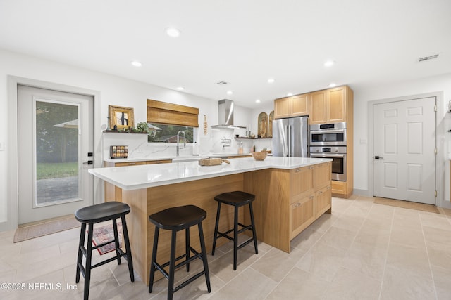 kitchen featuring a large island, sink, wall chimney exhaust hood, stainless steel appliances, and a breakfast bar