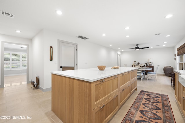 kitchen with ceiling fan, a kitchen island, light stone counters, and light tile patterned floors