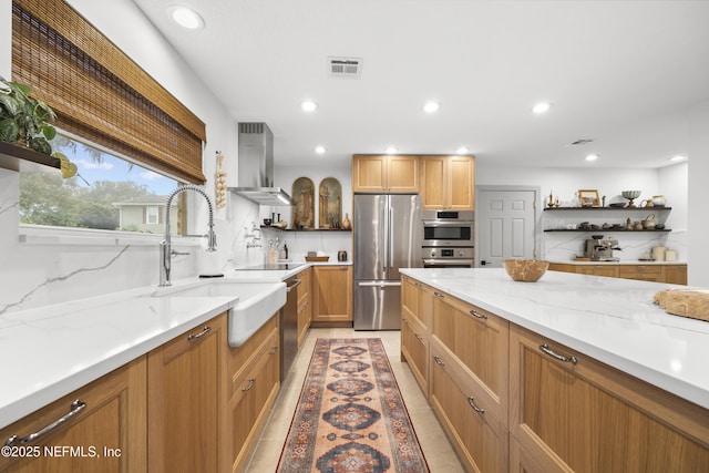 kitchen featuring light stone countertops, sink, wall chimney range hood, light tile patterned flooring, and appliances with stainless steel finishes