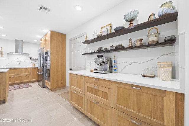 kitchen with wall chimney exhaust hood, decorative backsplash, light tile patterned floors, light stone counters, and stainless steel double oven