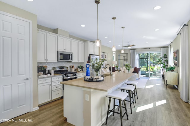 kitchen with a kitchen bar, stainless steel appliances, decorative light fixtures, white cabinetry, and an island with sink