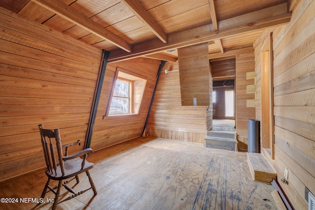 unfurnished living room featuring beam ceiling, wooden ceiling, a healthy amount of sunlight, and wooden walls