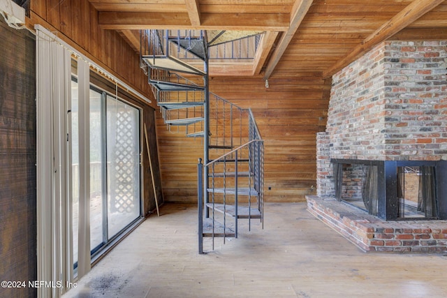 unfurnished living room with beam ceiling, hardwood / wood-style flooring, a brick fireplace, and wooden walls