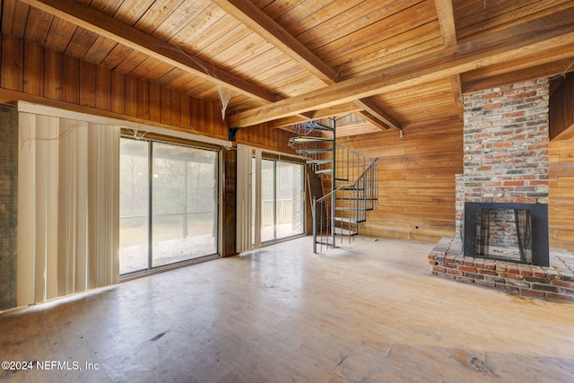 unfurnished living room featuring wood walls, beamed ceiling, and a brick fireplace