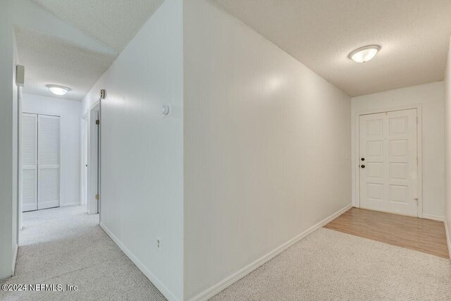 corridor featuring lofted ceiling, light colored carpet, and a textured ceiling