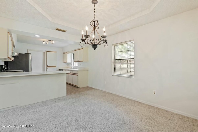 kitchen with light colored carpet, a tray ceiling, an inviting chandelier, stainless steel refrigerator, and hanging light fixtures