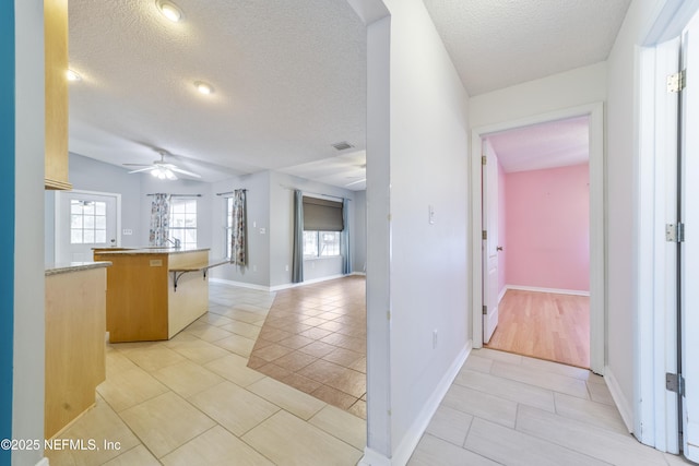 kitchen with a textured ceiling, ceiling fan, light tile patterned flooring, and a breakfast bar