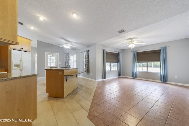 kitchen featuring a textured ceiling, ceiling fan, white fridge with ice dispenser, and a kitchen bar