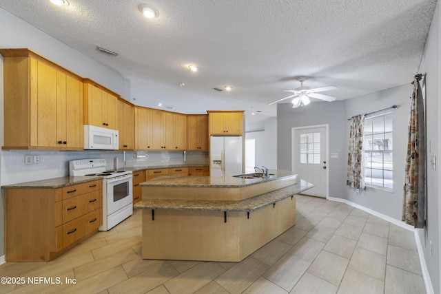 kitchen featuring white appliances, a textured ceiling, sink, a kitchen island with sink, and a breakfast bar