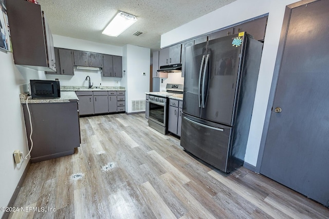 kitchen with light countertops, appliances with stainless steel finishes, a sink, and under cabinet range hood