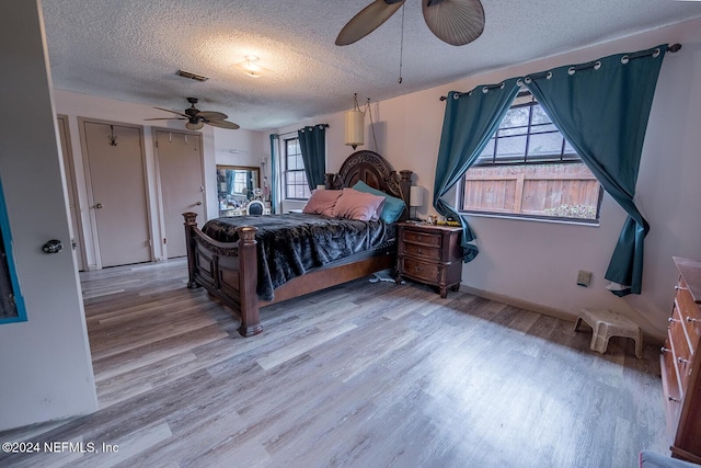 bedroom with a textured ceiling, light wood-type flooring, visible vents, and a ceiling fan