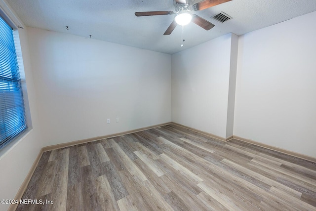 spare room featuring visible vents, light wood-style floors, ceiling fan, a textured ceiling, and baseboards