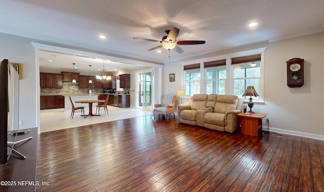 living room with dark hardwood / wood-style flooring, ceiling fan with notable chandelier, and ornamental molding