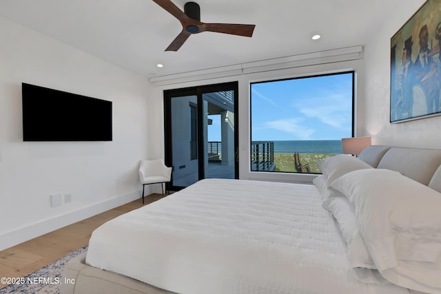 bedroom featuring access to exterior, hardwood / wood-style floors, a water view, and ceiling fan