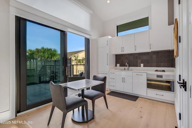 kitchen with white cabinets, stainless steel oven, backsplash, and light hardwood / wood-style flooring