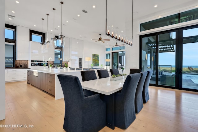 dining area featuring ceiling fan, light wood-type flooring, a towering ceiling, and a wealth of natural light