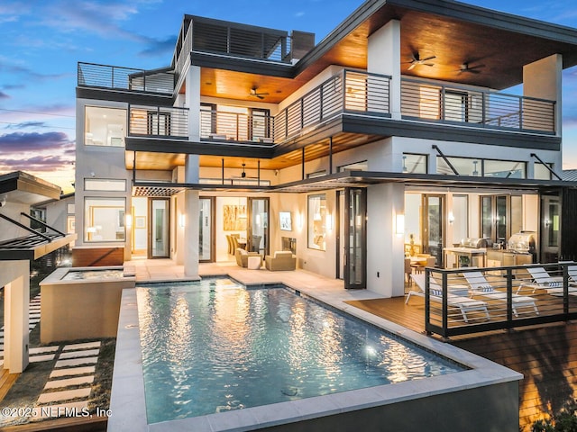 back house at dusk with an outdoor living space, ceiling fan, a balcony, and a swimming pool side deck