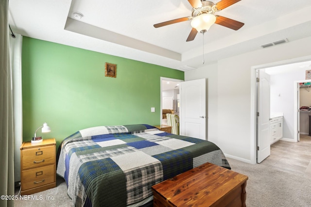 carpeted bedroom with a tray ceiling, ensuite bath, and ceiling fan