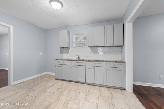 kitchen with backsplash, sink, light hardwood / wood-style flooring, light stone countertops, and a textured ceiling