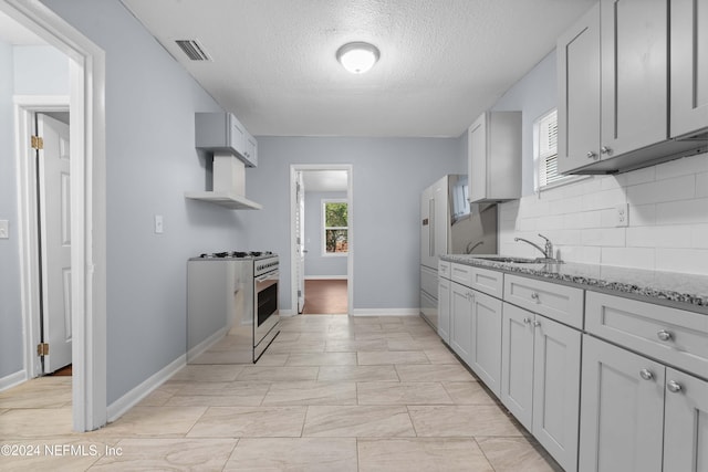 kitchen with decorative backsplash, light stone counters, gray cabinetry, a textured ceiling, and stainless steel gas stove