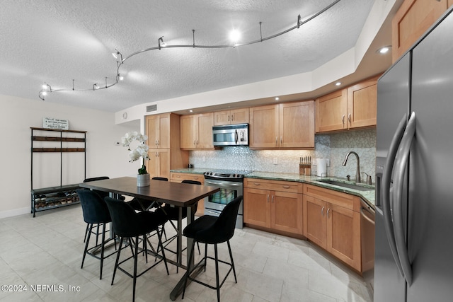 kitchen featuring a kitchen bar, appliances with stainless steel finishes, a textured ceiling, and sink