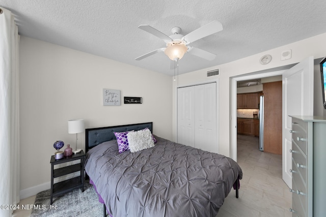 bedroom with ceiling fan, a textured ceiling, stainless steel refrigerator, and a closet