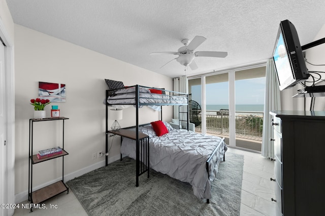 bedroom featuring access to outside, ceiling fan, a textured ceiling, and a wall of windows