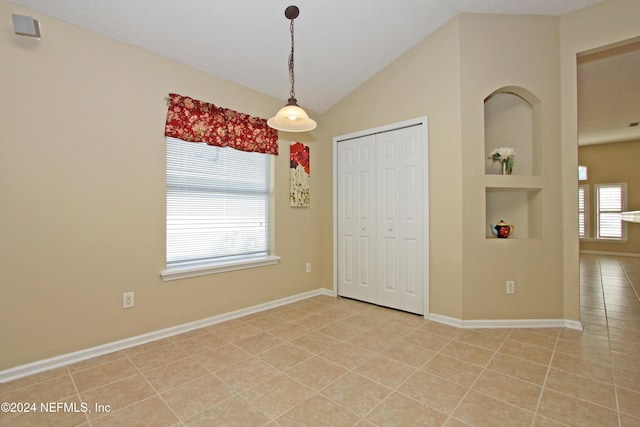 tiled empty room featuring lofted ceiling and built in shelves