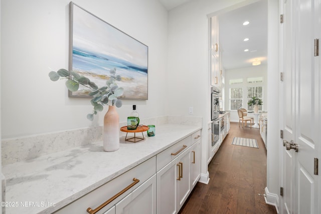 bar featuring light stone countertops, dark hardwood / wood-style flooring, white cabinets, and double wall oven