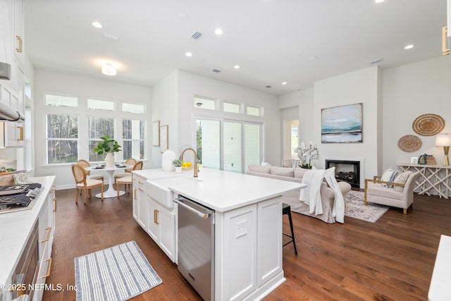 kitchen with dark wood-type flooring, a center island with sink, a kitchen breakfast bar, appliances with stainless steel finishes, and white cabinetry