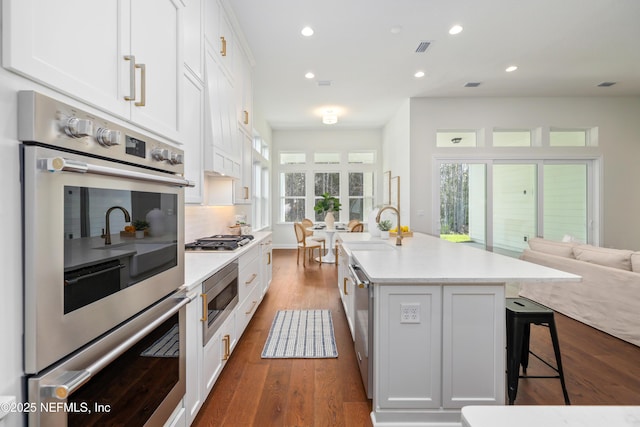 kitchen featuring a center island with sink, white cabinetry, a breakfast bar area, and appliances with stainless steel finishes