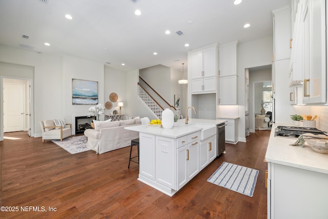 kitchen featuring sink, dark wood-type flooring, stainless steel appliances, a center island with sink, and white cabinets