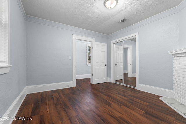 unfurnished bedroom featuring dark hardwood / wood-style floors, ornamental molding, a textured ceiling, a fireplace, and a closet