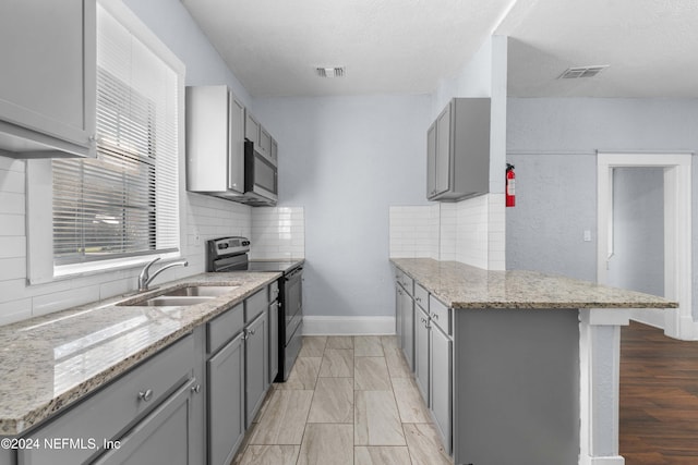 kitchen featuring gray cabinets, stainless steel appliances, light stone counters, and sink