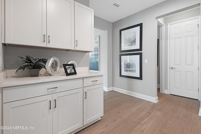 kitchen with white cabinets, light hardwood / wood-style floors, and light stone counters