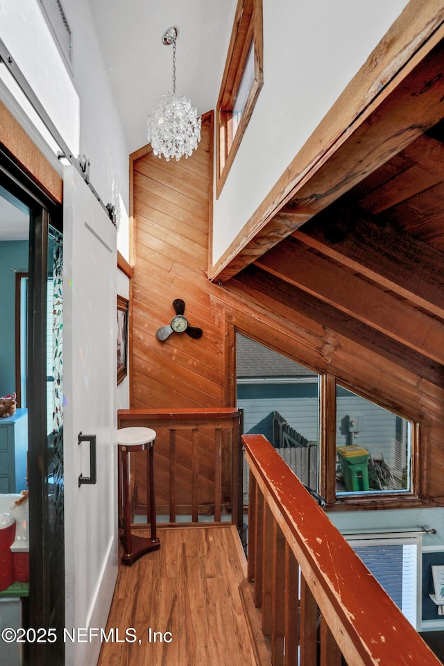 corridor with lofted ceiling, wooden walls, hardwood / wood-style flooring, a barn door, and a chandelier