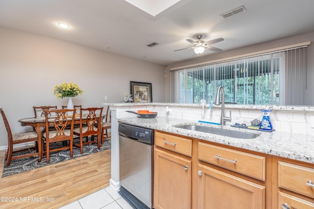 kitchen featuring stainless steel dishwasher, ceiling fan, light stone counters, and sink