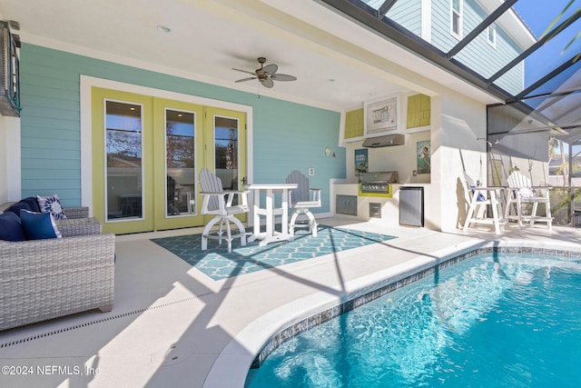 view of swimming pool featuring an outdoor kitchen, area for grilling, a lanai, ceiling fan, and a patio