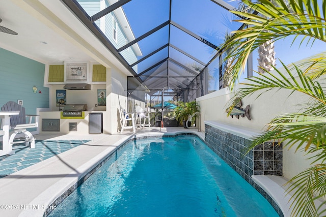 view of swimming pool featuring grilling area, pool water feature, a lanai, exterior kitchen, and a patio