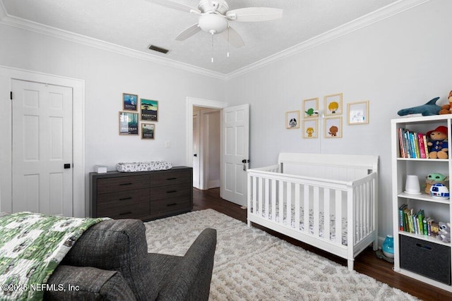 bedroom featuring a nursery area, dark hardwood / wood-style floors, ceiling fan, and ornamental molding