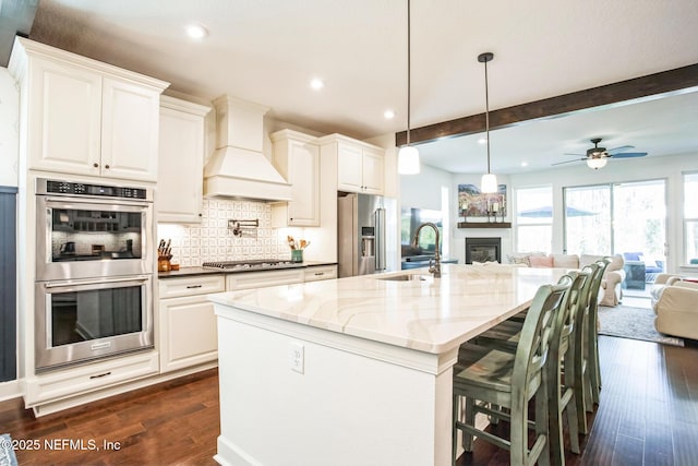 kitchen with dark stone counters, custom range hood, stainless steel appliances, sink, and white cabinets