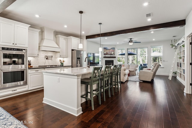 kitchen featuring ceiling fan, white cabinetry, beamed ceiling, custom exhaust hood, and appliances with stainless steel finishes